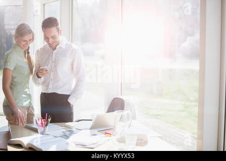 Happy young businessman and businesswoman using mobile phone at office desk Banque D'Images