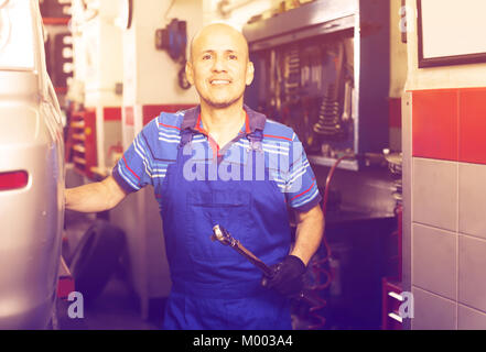 Heureux homme mature technicien en salopettes debout dans l'atelier de voiture Banque D'Images