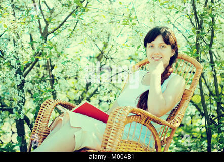 Girl reading book dans le jardin en fleurs Banque D'Images