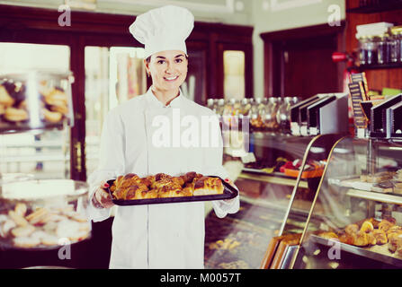 Smiling happy woman baker montrant au chaud délicieux croissants dans une boulangerie Banque D'Images