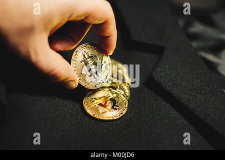 Hand holding coin Bitcoin sur un tas de pièces d'or sur un costume d'affaires Banque D'Images