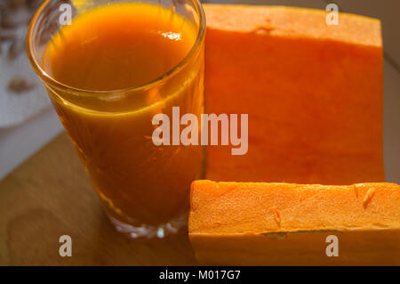 La citrouille smoothie dans un verre et de citrouille crues coupées sur fond de bois Banque D'Images