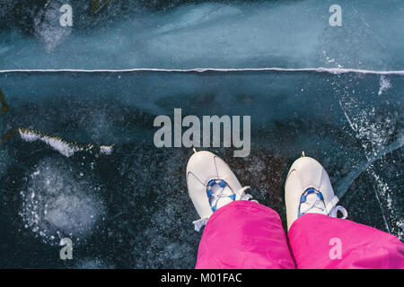 Fille d'un patineur en patins et rose vintage pantalon de ski patins sur la glace transparente bleu fée magnifique du lac Baikal avec des fissures et de la neige. Banque D'Images