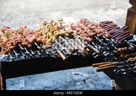 De nombreuses matières premières brochettes de viande de porc et de veau et de pommes de terre crues avec du bacon. À côté il y a une brochette de saucisses et des shish kebabs. Banque D'Images