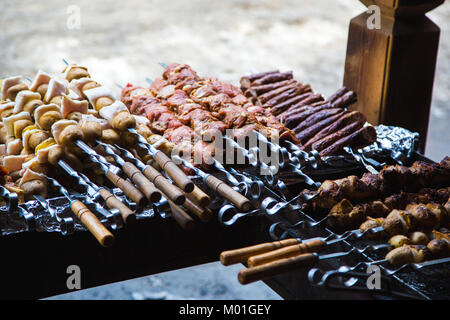 De nombreuses matières premières brochettes de viande de porc et de veau et de pommes de terre crues avec du bacon. À côté il y a une brochette de saucisses et des shish kebabs. Banque D'Images