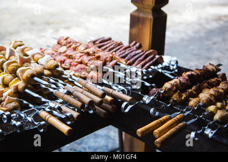 De nombreuses matières premières brochettes de viande de porc et de veau et de pommes de terre crues avec du bacon. À côté il y a une brochette de saucisses et des shish kebabs. Banque D'Images