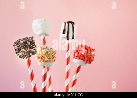 Sweet moelleux marshmallow et sucettes sur paille décoré avec du chocolat fondu et des gâteaux Sprinkles sur fond rose. Les enfants adoreront ces décisions. Cop Banque D'Images