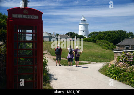 Trois touristes regardant le phare désaffecté blanc au centre de l'île de St Agnes, Penzance, Cornwall, Royaume-Uni. Banque D'Images