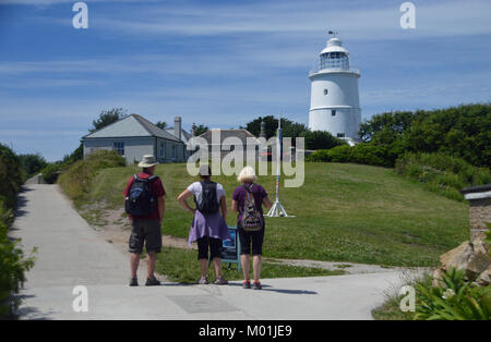 Trois touristes regardant le phare désaffecté blanc au centre de l'île de St Agnes, Penzance, Cornwall, Royaume-Uni. Banque D'Images