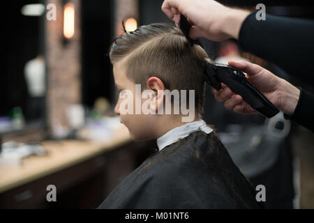 Petit garçon sur une coupe dans le salon de coiffure est assis sur une chaise. Banque D'Images