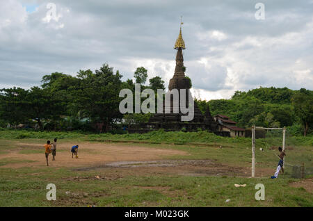 Mrauk-U, l'État de Rakhine / Myanmar - 18 octobre 2016 : les garçons jouent au football sur un terrain boueux en face d'une ancienne pagoda Banque D'Images