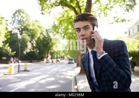 Jeune homme d'affaires sur le téléphone dans la rue, en attente de taxi Banque D'Images