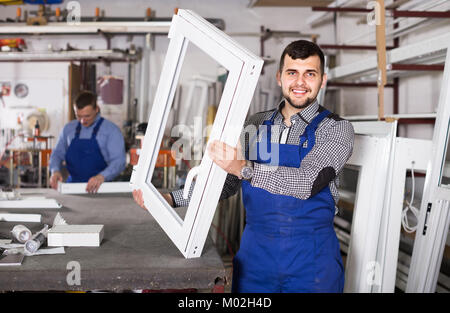 Les salariés de production en combinaison avec différents profils PVC fini et windows en usine Banque D'Images