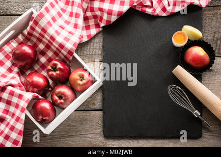 Pommes rouges bien mûrs en bouleau-box sur planche de bois avec une serviette autour de rouge à carreaux et accessoires pour la cuisson. Banque D'Images
