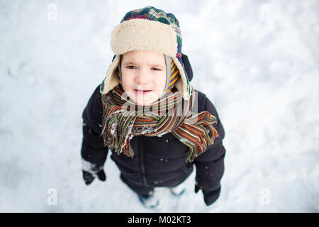 Vue de dessus d'un malheureux petit enfant dans des vêtements chauds, et l'air renfrogné. Garçon bouleversé dans la neige. Banque D'Images