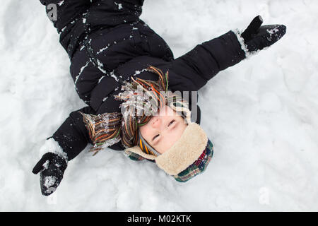 Vue de dessus d'un petit enfant vêtu de vêtements chauds avec les bras étendus de large dans la neige. Garçon faire un ange. Banque D'Images