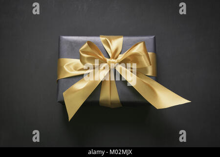 Boîte-cadeau enveloppé dans du papier noir avec du ruban d'or sur la surface noire. Vue d'en haut. Banque D'Images