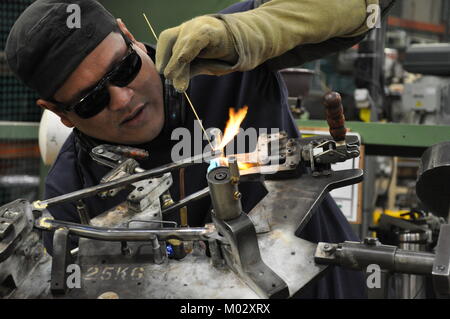 Soudeur travaillant sur cadre du vélo en acier dans une usine britannique avec flamme visible et portant des lunettes de brasage Banque D'Images