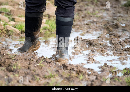 Une femme marche à travers la boue épaisse sur sol humide détrempée. Elle porte des bottes wellington. la boue est à la cheville dans les lieux d'où la difficulté à marcher Banque D'Images