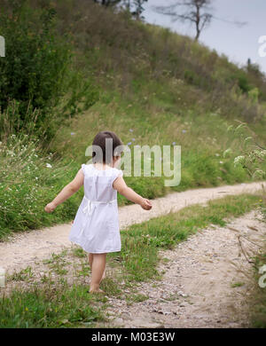 Un enfant marche pieds nus sur le chemin de sable robe blanche et pieds nus le sable de la route Banque D'Images