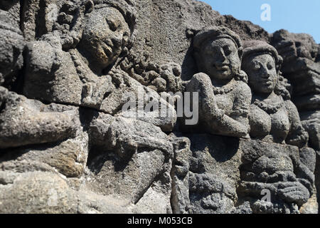 Mur libre ornée de bas-reliefs représentant des scènes de la vie de l'ancienne Java et les visages. La sculpture sur pierre très détaillées. Bouddhiste de Borobudur Banque D'Images