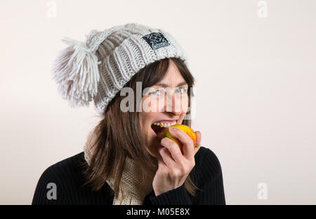 Vue rapprochée isolée de la femme en hiver chapeau de galet mangeant de la pomme à l'intérieur avec fond blanc. Banque D'Images