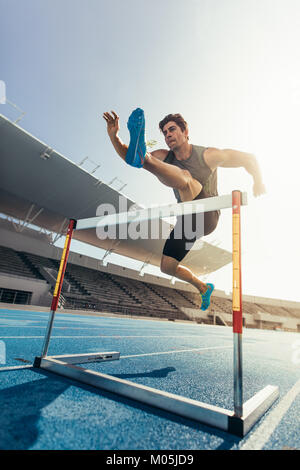 Runner sautant par-dessus un obstacle lors d'événements d'athlétisme. L'exécution d'un athlète course de haies dans un stade. Banque D'Images