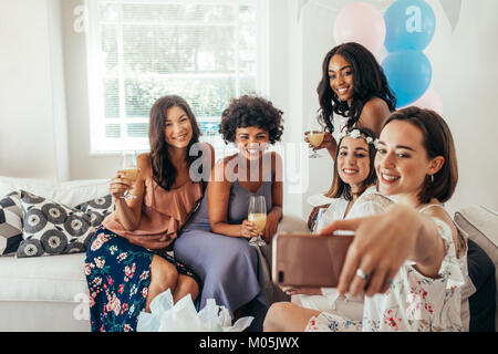 Groupe d'amis divers femmes à avoir du plaisir de prendre de douche de bébé avec un téléphone mobile selfies et souriant. Banque D'Images