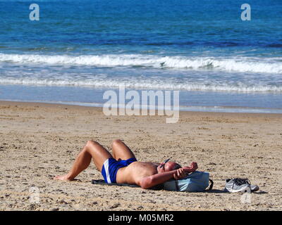 Les loisirs en vacances - Un homme se fait bronzer sur le couché de soleil à la plage Banque D'Images