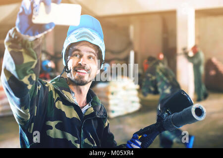 Jeune homme dans le masque bleu fait sur le champ de bataille de selfies paintball club. Banque D'Images