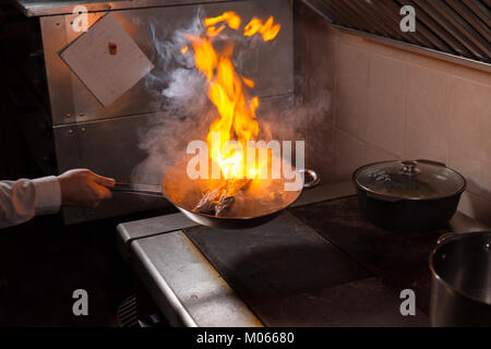 Rôti de côte d'agneau flambé. Avec le feu de cuisson dans une poêle. Chef professionnel dans une cuisine commerciale la cuisson. L'homme grande friture dans la casserole sur feu de cuisson en slow motion cuisine extérieure. Banque D'Images