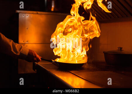 Rôti de côte d'agneau flambé. Avec le feu de cuisson dans une poêle. Chef professionnel dans une cuisine commerciale la cuisson. L'homme grande friture dans la casserole sur feu de cuisson en slow motion cuisine extérieure. Banque D'Images