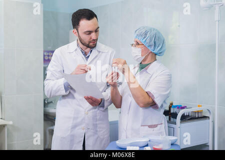 Les jeunes et les cadres supérieurs de chimistes travaillant ensemble et à la recherche à un tube à essai dans un laboratoire clinique Banque D'Images
