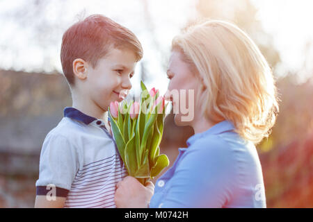 Happy little fils donne bouquet de tulipes pour maman à la fête des Mères au coucher du soleil Banque D'Images