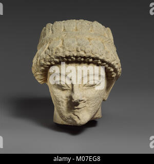 Cette tête en calcaire présente une figure masculine sans barbe avec une couronne de feuilles, illustrant des techniques artistiques classiques, une sculpture détaillée et la représentation de traits humains dans la sculpture antique. Banque D'Images