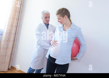 Femme enceinte se penchant en arrière contre ball aérobie Banque D'Images