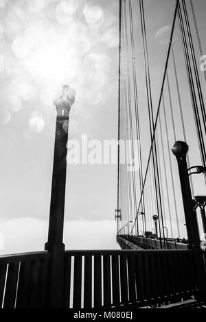 Golden Gate Bridge sur l'épais brouillard, ci-dessous, avec sun flare qui rebondissent sur un lampadaire sur le pont. Vue en gros plan. Monochrome noir et blanc. Banque D'Images