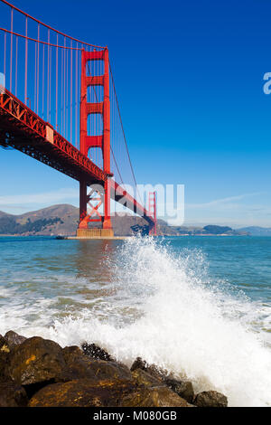 Golden Gate Bridge vu du dessous avec des projections d'une vague de l'océan dans l'avant-plan. Banque D'Images