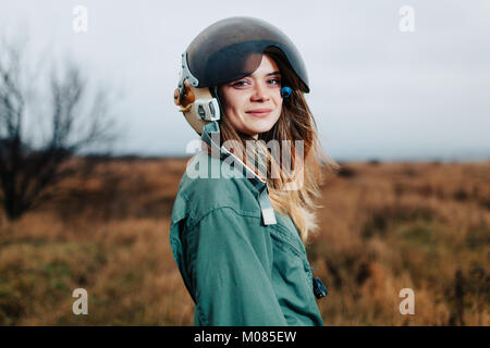 Belle femme pilote d'avion dans le coucher du soleil permanent en uniforme sur le terrain avec casque Banque D'Images