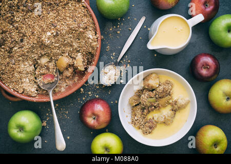 Crumble aux pommes, crème anglaise et pommes fraîches sur un fond d'ardoise Banque D'Images