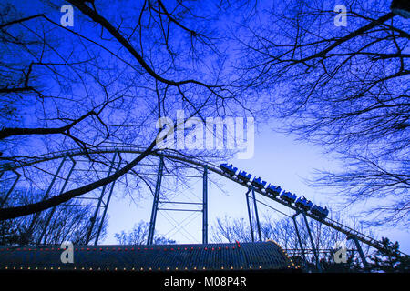 Vue grand angle d'une montagne russe dans un parc à thème avec des branches et de ciel bleu. un peu de bruit et grain. Banque D'Images