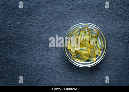 Petit bol en verre rempli d'huile de poisson capsules gel contre une pierre sombre contexte Banque D'Images