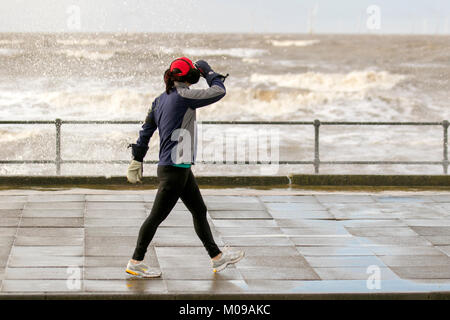 Femme en train de courir sur la promenade du front de mer à Crosby, Merseyside. 19th janvier 2018. Météo Royaume-Uni. Stormy Seas sur la promenade côtière de Sefton où les gales continuent à batter la côte. Crédit : MediaWorldImages/Alamy Live News Banque D'Images