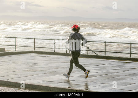 Femme en train de courir sur la promenade du front de mer à Crosby, Merseyside. 19th janvier 2018. Météo Royaume-Uni. Stormy Seas sur la promenade côtière de Sefton où les gales continuent à batter la côte. Crédit : MediaWorldImages/Alamy Live News Banque D'Images