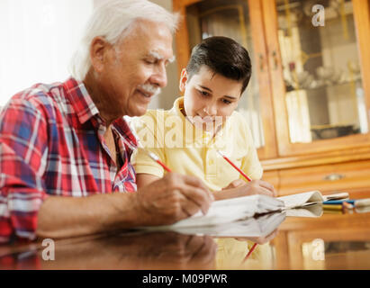 Petit garçon de l'école de faire ses devoirs avec Vieil Homme à la maison Banque D'Images