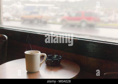 Une tasse de café sur une table en bois avec cendrier, près d'une fenêtre, rétro, style du film. Banque D'Images