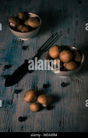 Photo verticale avec des champignons comestibles. Les champignons avec brown caps dans deux bols et sur vintage blue planche de bois. Grande décision placé entre les coupes. Bleu à sec Banque D'Images