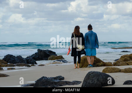 Des couples Soirée Beach à pied. L'homme et la femme se tenir par les rochers sur la plage à la recherche pour voir. Des couples balade romantique le long de mer. Banque D'Images