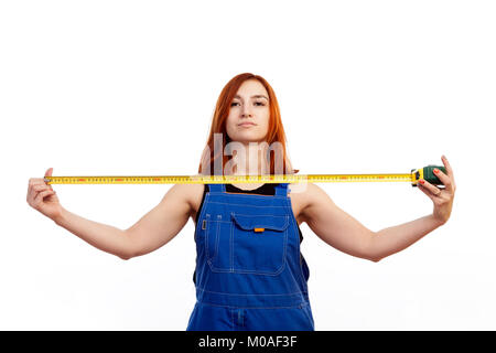 Une jeune femme rousse dans un T-shirt noir et bleu dans l'ensemble de la construction est titulaire d'une règle de type sur un fond isolé blanc Banque D'Images