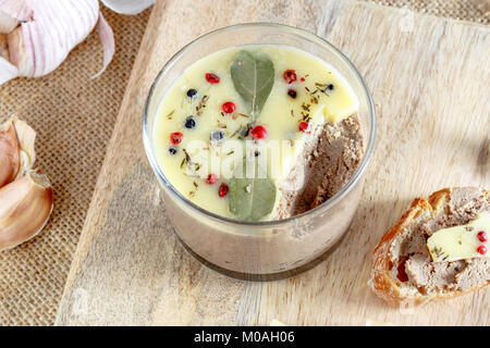 Le pâté de foie de poulet couverts avec du beurre fondu et décoré avec les feuilles de laurier et du poivre noir et rouge rustique sur conseil. Banque D'Images